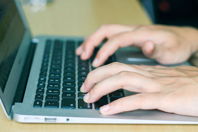 Cropped hands of person using laptop on wooden table