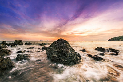 Rocks at beach against cloudy sky during sunset