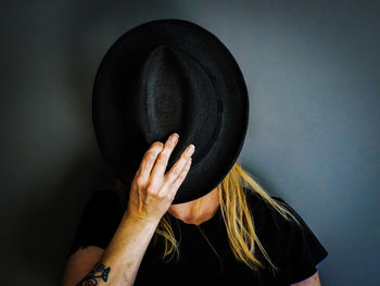 Woman with face covered by hat against wall