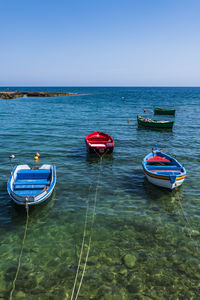 Boats moored in sea against clear blue sky
