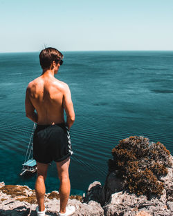 Rear view of shirtless man looking at sea against sky