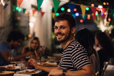 Portrait of smiling young man having dinner with friends during garden party