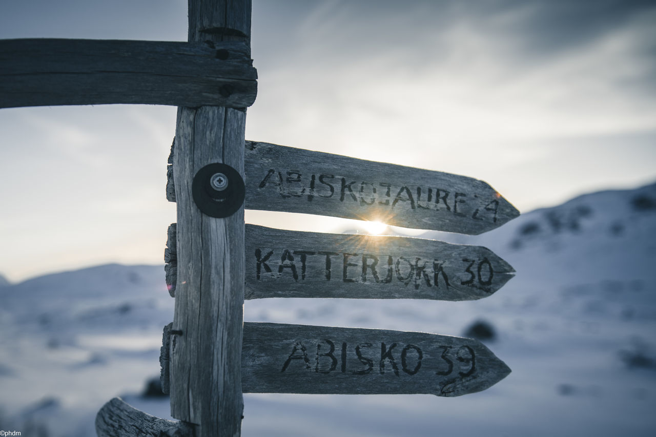 communication, snow, sky, text, sign, winter, nature, cloud, mountain, guidance, blue, western script, no people, wood, directional sign, symbol, white, road sign, landscape, cold temperature, outdoors, tranquility, mountain range, scenics - nature, focus on foreground, arrow symbol, beauty in nature, information sign