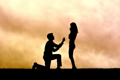 Silhouette man with engagement ring proposing to girlfriend against sky during sunset