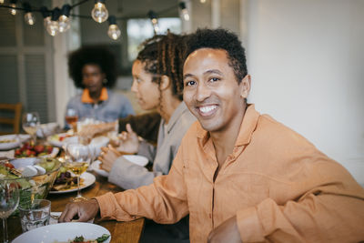 Portrait of smiling man sitting at dining table during dinner party in patio