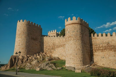 Street and light posts beside stone towers in the large wall encircling the town of avila, in spain.