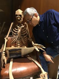 Man looking at newspaper by human skeleton on chair