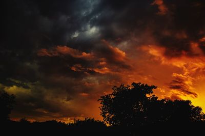 Low angle view of silhouette trees against dramatic sky