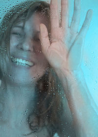 Close-up of smiling woman taking shower seen through glass