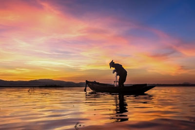 Silhouette man in boat against sky during sunset