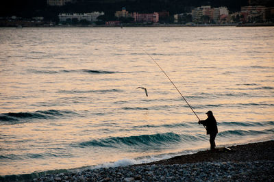 Silhouette man fishing at beach against sky