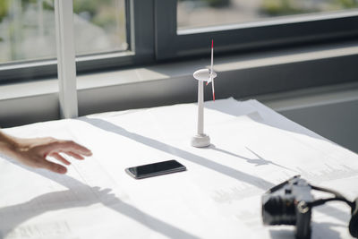 Hand of man reaching for smartphon lying on desk with blueprints and wind wheel