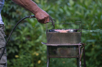 Midsection of man blowing barbecue grill with equipment while preparing food