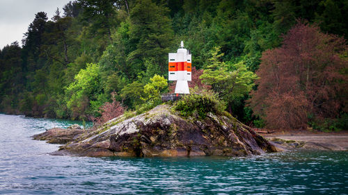 Lighthouse amidst trees and buildings by sea