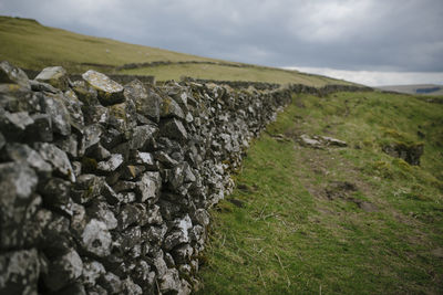 Stone wall on landscape against cloudy sky