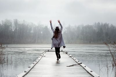 Woman waving her hands in the air walking along a jetty at the beach