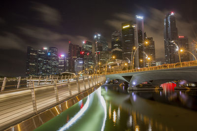 Illuminated bridge over river amidst buildings in city at night