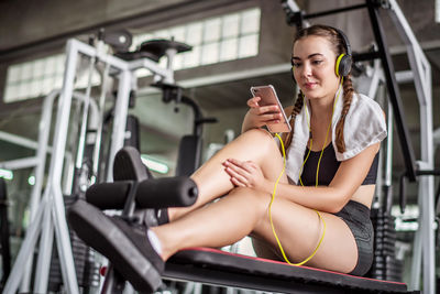 Young woman listening to music while sitting in gym
