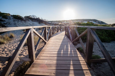 Wooden bridge leading towards mountain against sky