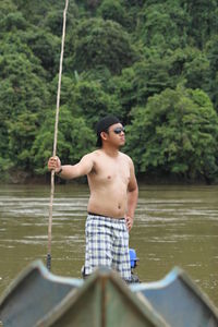 Full length of shirtless man standing in lake against trees