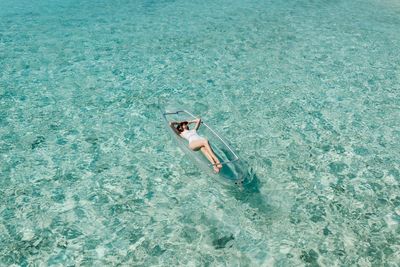 High angle view of young woman lying in boat on sea during sunny day