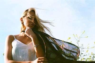 Low angle view of woman with scarf against sky on windy day