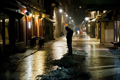 Man walking on wet street in illuminated city at night