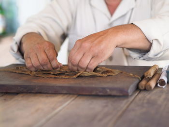 Midsection of man making cigars at table
