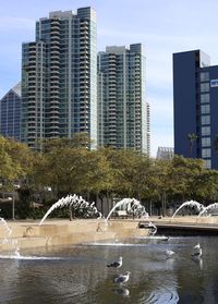 Modern buildings by river against sky in city