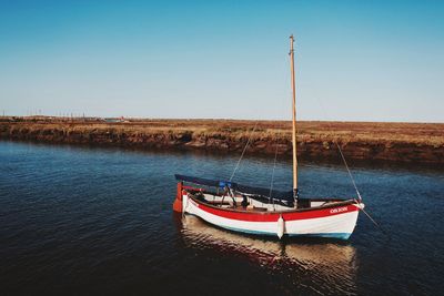 Boat moored on shore against clear blue sky
