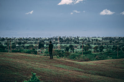 Rear view of man standing on field against sky