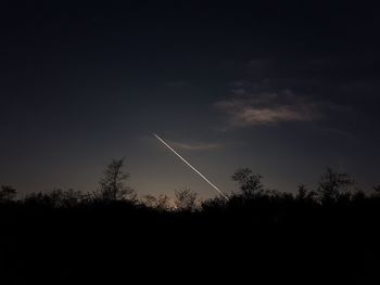 Silhouette trees against vapor trail in sky