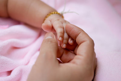 Close-up of parent holding baby hand on bed