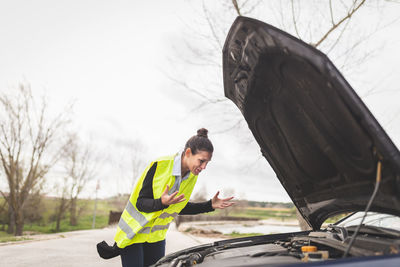 Woman looking at car engine, she doesn't know what to do, car broken down in the middle of the road.