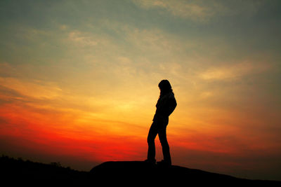 Silhouette woman standing on rock against sky during sunset