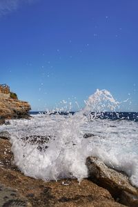 Sea waves splashing on rocks against clear blue sky