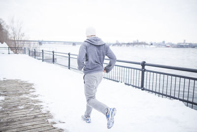 Rear view of man standing on railing by lake during winter