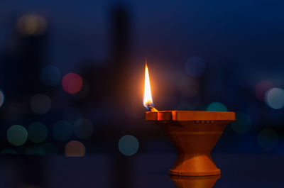 Selective focus on flame of clay diya lamp with colorful city bokeh lights. diwali festival concept.