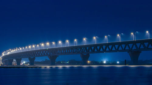 Illuminated bridge over river against sky at night