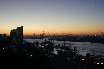 Silhouette city by sea against sky during sunset