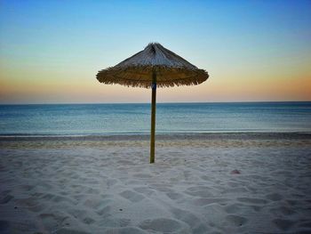Thatched roof umbrella at beach against clear sky during sunset