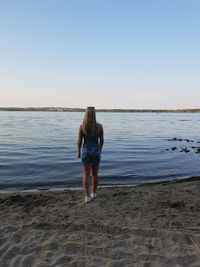 Rear view of woman standing on beach against clear sky