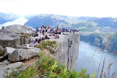 People on rocks by mountains against sky