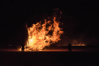 Silhouette man standing by bonfire against sky at night