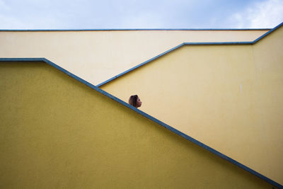 Low angle view of woman against yellow wall of building