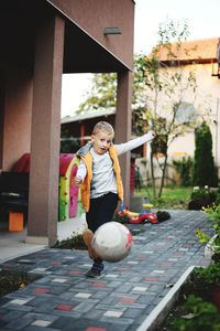 Full length portrait of cute boy kicking ball outside house