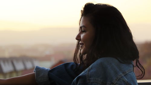 Portrait of young woman looking away against sky during sunset