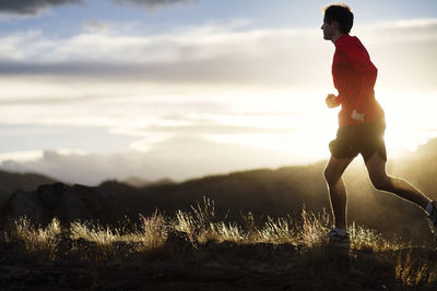 Side view of male athlete running on grass field during sunset