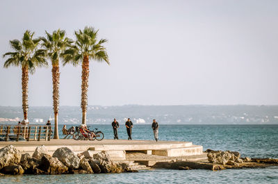 People standing on rock by sea against clear sky