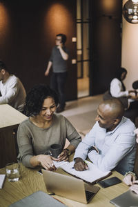 Smiling mature woman discussing over laptop with male colleague at desk in creative office